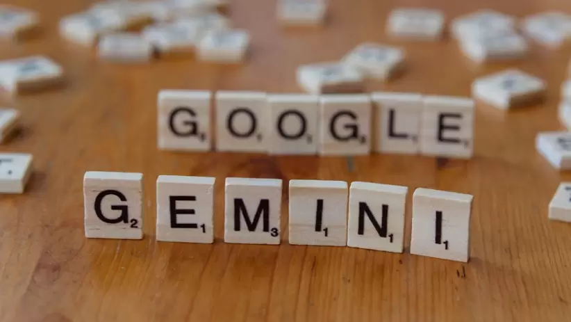 Fichas de Scrabble que forman las letras Google y Gemini sobre una mesa de madera, centrándose en conceptos de IA.