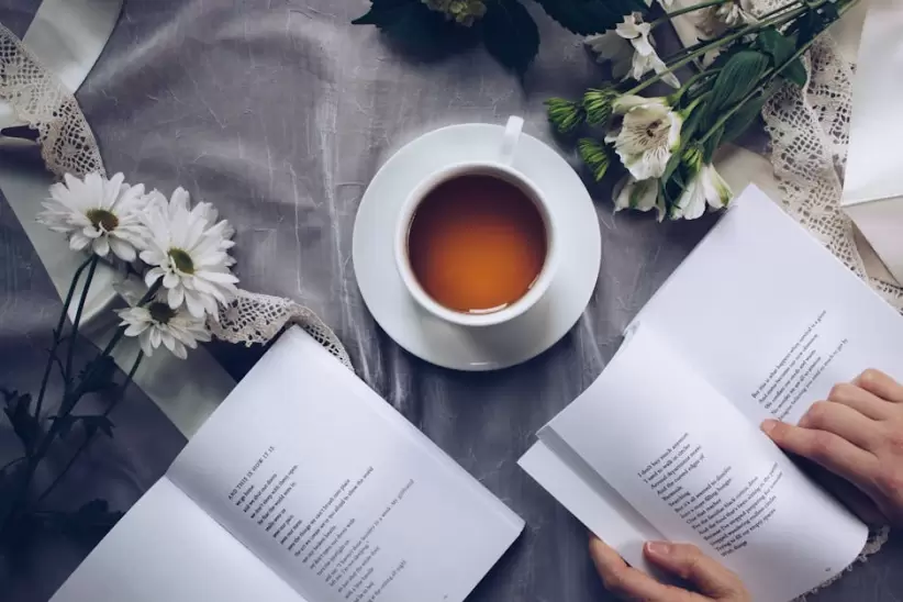 Taza De Té De Cerámica Blanca Con Platillo Cerca De Dos Libros Sobre Textil Floral Gris